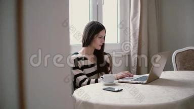 女士使用笔记本电脑，在明亮的餐厅享用早间咖啡。 透过敞开的门观看